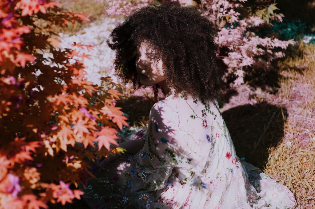 A feminine figure crouches in some foliage, face partially obscured by shadows.