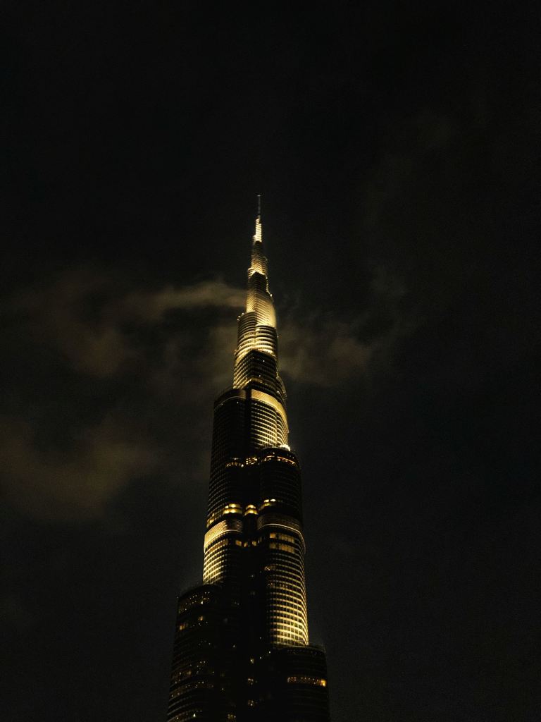 A tower, lit up at night, reaching into the clouds.